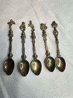 Five silver-plated souvenir spoons laid out showing figural tops and bowls