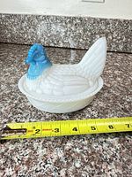 Side view of milk glass hen on nest with measuring tape showing size