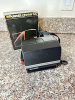 Front angled view of Polaroid Sun 600 camera with original box visible behind