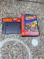 Game Genie adapter next to ToeJam & Earl clamshell case front