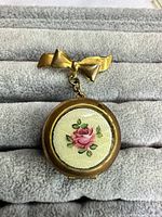 Front view of closed locket brooch showing bow hanger and enamel rose motif
