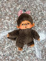 Front view of brown Monchhichi doll with vinyl face, hands, feet, pink bow