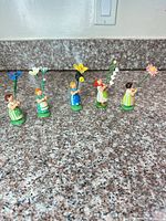Five wooden girl figurines holding flowers lined up on counter