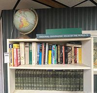Overall view showing globe atop shelf, atlas, assorted books, encyclopedias