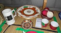 Group view showing large orange decorative plate, oversized mug, stack of Coalport cups and saucers, small Royal Crown Derby dish