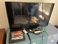 TV with remote, cables and two DVD movies on cabinet
