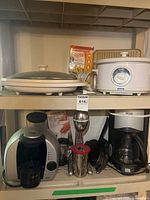 Overall view of shelving contents showing slow cooker, electric grill, Tassimo machine, milkshake mixer, DeLonghi coffee maker and cookware