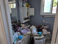 Wide view of bathroom showing cabinet with assorted toiletries, plastic drawer unit, organizer baskets and paper products