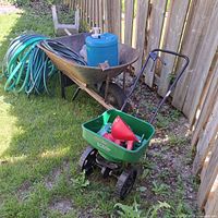 Overall view of wheelbarrow, hoses, blue container, Scotts spreader on grass