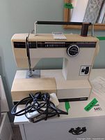 Front view of Omega sewing machine showing stitch selector dial, 12-stitch panel, attached foot pedal cord