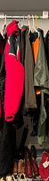 Multiple jackets and outerwear pieces hanging on rod, colors red, black, olive, orange visible