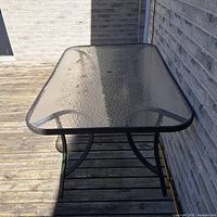 Front view of glass patio table showing top, frame, umbrella hole