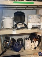 Shelf with crock pot, Foreman grill, waffle maker in foam, mixing bowl, teapot, Bravetti appliance, toaster, manual processor visible