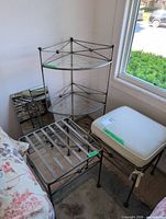 Corner steel plant stand with three glass shelves alongside two steel stools and cushion