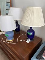 Three table lamps on dresser: two cobalt blue glass with pleated shades, one light blue ceramic with white shade