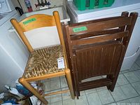 Light-finish chair and two folded dark-finish chairs beside appliance