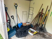 Overall view of shovels, rakes, broom, tarp, tray in shed