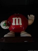Front view of red M&M candy dispenser showing logo, face and dispensing hole
