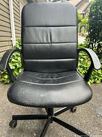 Front view of black faux leather office chair showing armrests, seat wear and caster base