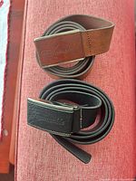 Brown and black Faconnable leather belts coiled, showing buckles
