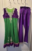 Full view of sleeveless green and purple Anarkali kameez with matching purple salwar pants hanging