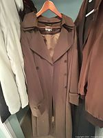 Full view of brown trench coat on hanger in closet