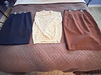 Front view of beige cardigan centered between black and brown skirts laid flat on bed