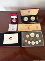 All three coin sets displayed: 2010 proof set, 1983 silver dollar, 1974 Tanzania coins with cases and COAs
