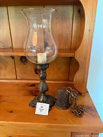 Hurricane lamp and cowbell displayed together on wooden shelf