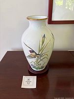 Front view of porcelain vase on stand showing bird motif and gold rim