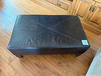Top and side view of ottoman showing overall form, leather surface, and wooden legs
