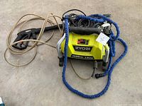 Front view of Ryobi pressure washer showing branding, power switch, PSI and GPM rating, cords and hoses