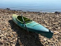 Full view of kayak on rocky beach with paddle across cockpit