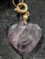 Front view of purple fluorite heart pendant showing carved figure and gold-tone bail