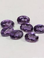Seven oval purple faceted gemstones on white background
