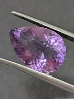 Front view of pear-cut amethyst held by tweezers