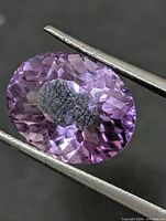 Front view of faceted oval amethyst held by tweezers
