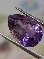 Front view pear-cut purple amethyst held by tweezers