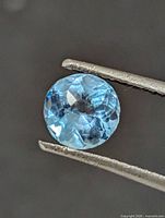 Close-up of round blue topaz held in tweezers