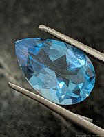 Pear-shaped blue topaz held in tweezers, full view