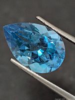 Front view of pear-cut blue topaz held by tweezers