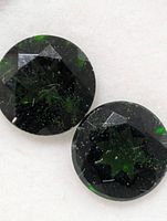 Close-up of two round green gemstones showing facets and inclusions