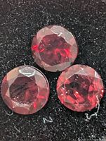 close-up of three round red garnet stones on black foam