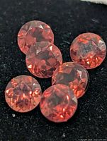 Six round orange-red faceted gemstones on black background