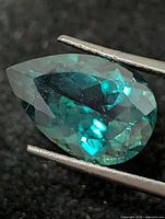 Front view of pear-cut green topaz held by tweezers