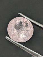 Front view of round pink faceted gemstone held by tweezers
