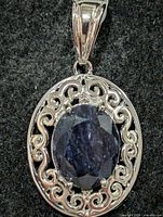 Front view of silver pendant showcasing dyed sapphire and scrollwork setting