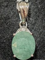 front view of silver pendant highlighting emerald and setting
