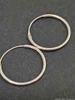Two thin sterling silver hoop earrings on dark background