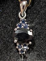 front view of silver pendant showing central oval sapphire and surrounding round sapphires